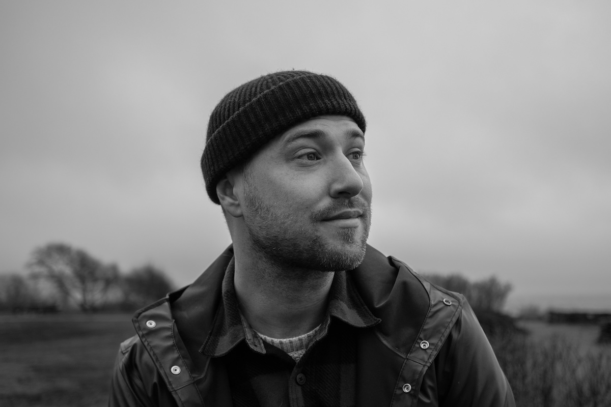 A portrait of Chris Goodwin on Maine's coast. He is wearing a hat and a rain jacket with a plaid undershirt.